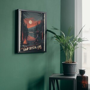 May include: A framed poster with a vintage aesthetic depicting a lake scene with a cabin, a campfire, and a full moon. The text on the poster reads "Stay at Camp Crystal Lake Est. 1955".