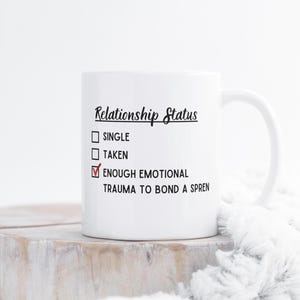 Op de afbeelding: Witte keramische mok met een zwart en rood ontwerp. De mok heeft de tekst "Relatiestatus" met een vinkje naast "Genoeg emotioneel trauma om een Sprend te binden".