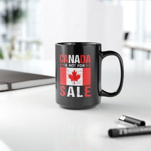 May include: Black ceramic coffee mug with a white graphic that says "CANADA IS NOT FOR SALE" with a red and white Canadian flag in the center.