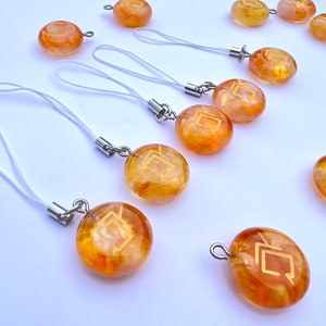 May include: A set of ten amber-colored glass charms with a gold geometric design. Each charm is attached to a white string with a silver ring.