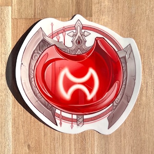 May include: A red and white sticker with a stylized symbol of a double-headed axe. The sticker is surrounded by a decorative border with a white background.