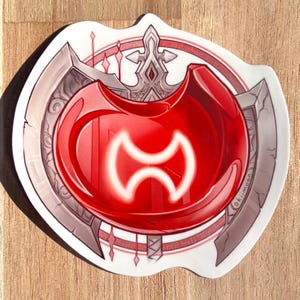 May include: A die-cut sticker featuring a large, glossy red circular gem with a glowing white double-axe symbol in the center. The gem is set against a background of a grey, ornate, metallic-looking axe head with intricate line work and details.