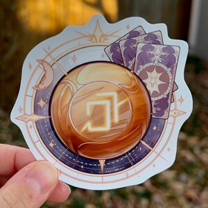Peut inclure: Un autocollant blanc avec un orbe dor&eacute;, une boussole et trois cartes de tarot violettes. L'orbe contient un carr&eacute; lumineux. La boussole a un croissant de lune et une &eacute;toile. Les cartes de tarot repr&eacute;sentent une &eacute;toile et un croissant de lune. L'autocollant est marqu&eacute; "okimoon" en bas.