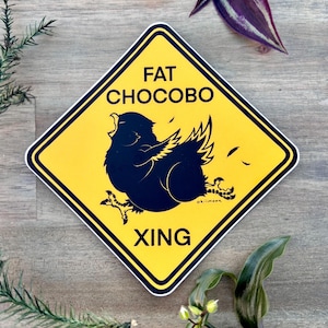 May include: A yellow diamond-shaped road sign with black text and a black silhouette of a large, round bird with wings spread. The text on the sign reads "FAT CHOCOBO XING".