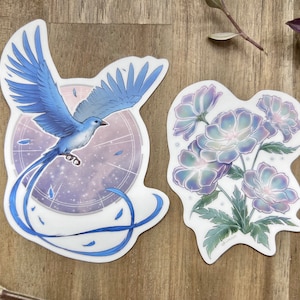 May include: Two sticker designs featuring a blue bird with a long tail and a cluster of purple flowers. The bird sticker has a celestial background with a circular design. The flower sticker has a white background with a green stem and leaves.