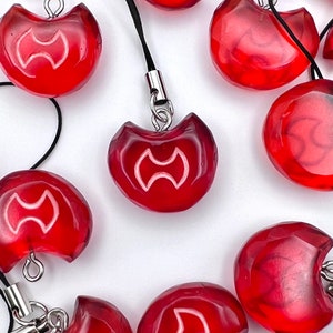 May include: A set of red, crescent-shaped charms with a white symbol. The charms have a hole at the top for attaching to a keychain or phone case.