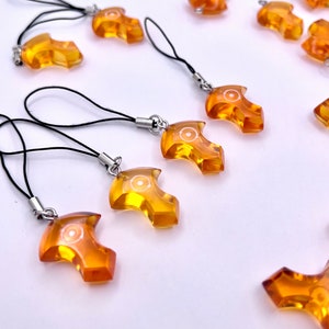 May include: A group of amber-colored keychains with a black string and a silver metal ring. Each keychain features a unique design with a white circle in the center.