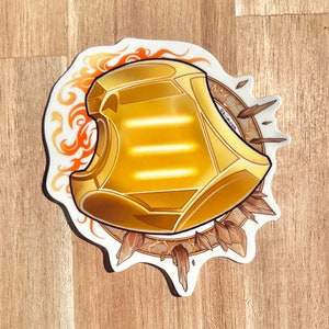 May include: A gold sticker with a stylized image of a helmet with three horizontal lines. The helmet is surrounded by a ring of flames and crystals.