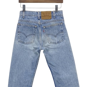 May include: Light blue denim jeans with a brown leather patch on the back pocket that says "Levi's" in white text. The jeans are hanging on a wooden hanger.