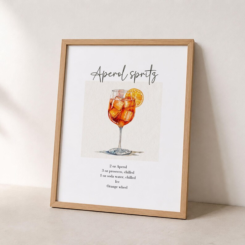 Pode incluir: Uma impress&atilde;o emoldurada com uma ilustra&ccedil;&atilde;o em aguarela de um Aperol Spritz num copo com uma rodela de laranja. O texto diz Aperol Spritz e lista os ingredientes: 2 oz Aperol, 3 oz prosecco, 1 oz &aacute;gua com g&aacute;s, gelo, rodela de laranja.