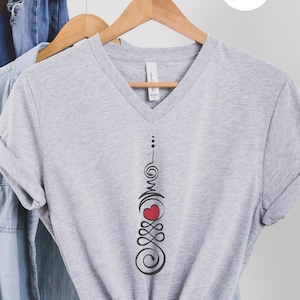 May include: A gray V-neck t-shirt with a black and red design. The design features a heart with a swirl pattern above and below it.