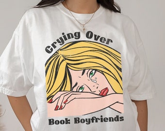 May include: White t-shirt with a graphic of a woman with blonde hair crying with the text "Crying Over Book Boyfriends" printed on it.