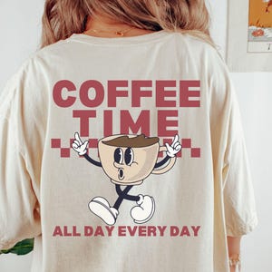 May include: A beige t-shirt with the text "Coffee Time" in red and a cartoon coffee cup with the text "All Day Every Day" in red.
