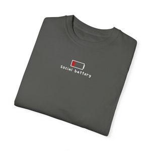 May include: A dark gray t-shirt with a white graphic of a low battery icon and the text "social battery".