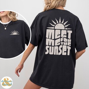 May include: Black oversized t-shirt with a white graphic print of a sun and the text "Meet Me For The Sunset".