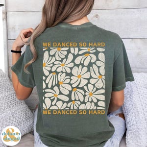 May include: A green t-shirt with a white daisy print and the text "We danced so hard" on the back.