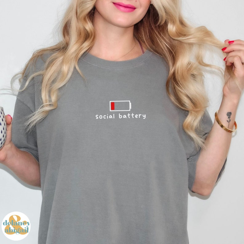 May include: Gray t-shirt with a white graphic of a low battery icon and the text "social battery".