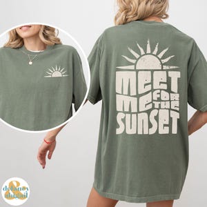 May include: An oversized green t-shirt with a vintage-style graphic print of a sun and the text "Meet Me For The Sunset".