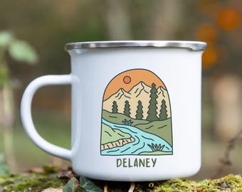 May include: White enamel camping mug with a colorful illustration of a mountain range, a river, and trees. The text "DELANEY" is printed on the bottom of the mug.