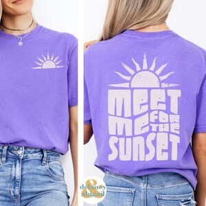 May include: Purple t-shirt with a white sun graphic and the text "Meet Me For The Sunset" on the back.