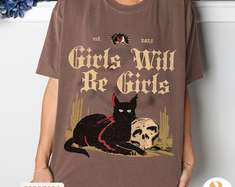 May include: Espresso-colored t-shirt with a graphic featuring a black cat, skull, and the text "Girls Will Be Girls." The design includes a stylized eye and the year 2025. The shirt is a relaxed fit.