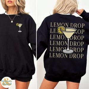 Pu&ograve; includere: Felpa nera con una grafica di martini al limone e il testo "Lemon Drop" ripetuto cinque volte sul retro.