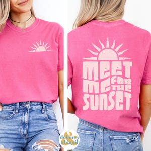 May include: Pink t-shirt with a white sun graphic on the front and the text "Meet me for the sunset" on the back.