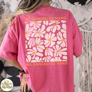 May include: Pink t-shirt with a white daisy print and the text "We danced so hard" in orange.