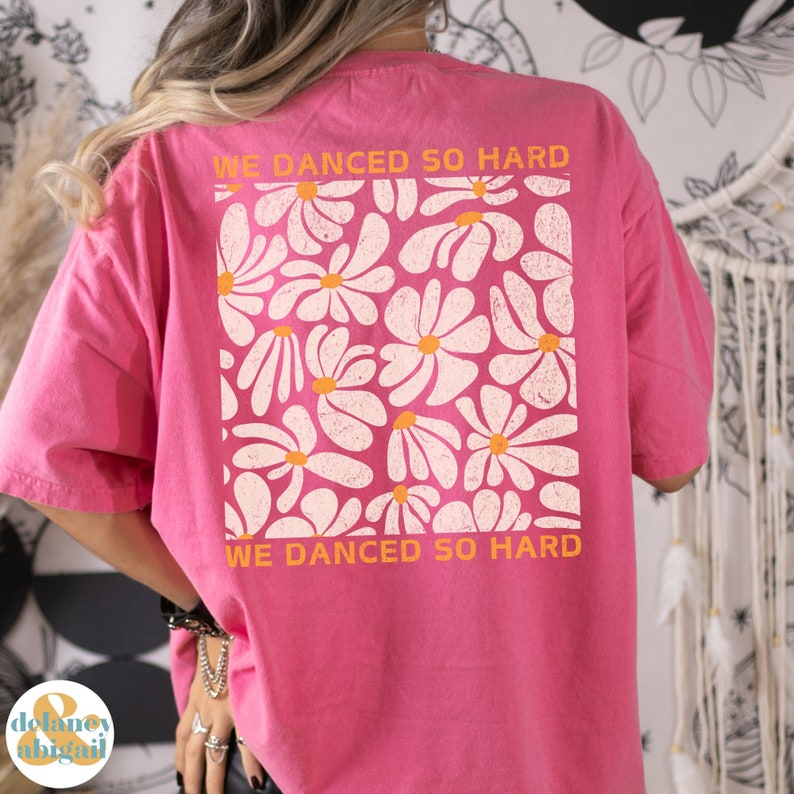 May include: Pink t-shirt with a white daisy print and the text "We danced so hard" in orange.