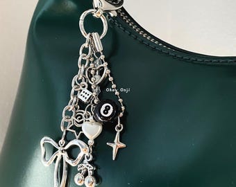 May include: A silver charm bracelet with a variety of charms, including a heart, a star, a dice, a cherry, a bow, and a black and white 8 ball charm. The bracelet is attached to a green leather handbag.