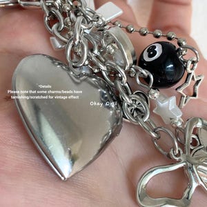 May include: A silver charm bracelet with a heart-shaped locket, a silver cross charm, a silver star charm, a silver butterfly charm, a black and white 8-ball charm, and a white bead charm. The bracelet has a silver chain and is adorned with various charms.