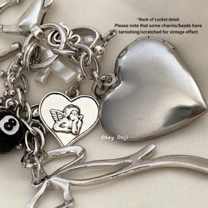 May include: A silver charm bracelet with a variety of charms, including a heart with an angel, a heart-shaped locket, a cross, and a 8 ball. The charms are attached to a silver chain.