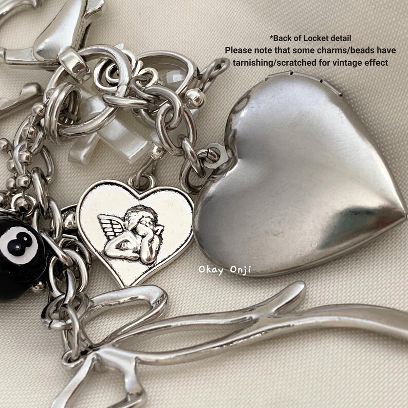 May include: A silver charm bracelet with a variety of charms, including a heart with an angel, a heart-shaped locket, a cross, and a 8 ball. The charms are attached to a silver chain.
