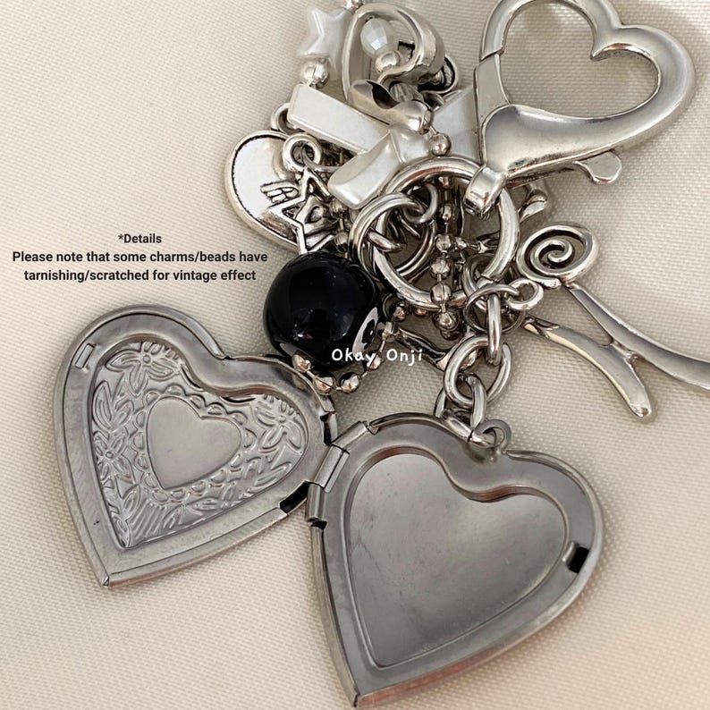 May include: A silver charm bracelet with a variety of charms, including hearts, a cross, a key, and a black bead. The bracelet has a vintage look with tarnished and scratched charms.