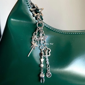 May include: A silver charm keychain with a star, butterfly, flower, tooth, and other charms hanging from a green leather handbag.