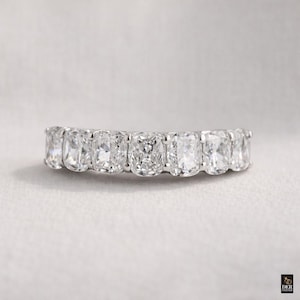 Può includere: Primo piano di un anello eternity di diamanti. L'anello presenta una serie di diamanti a taglio rettangolare, incastonati uno accanto all'altro, creando una fascia continua di brillantezza. I diamanti sono chiari e riflettono la luce.