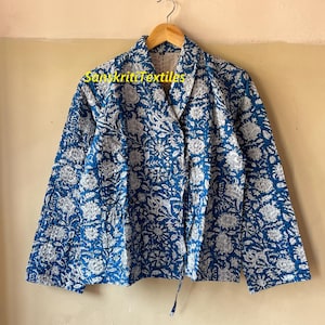 May include: A blue and white floral print jacket on a wooden hanger. The jacket features long sleeves and a tie closure. The text "Sanskriti Textiles" is visible on the jacket.