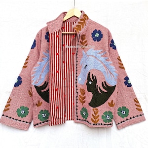 Könnte beinhalten: Rosa Jacke mit geometrischem Muster und gestickten Pferde- und Blumendesigns. Die Jacke hat ein rot-weiß gestreiftes Innenfutter und den Text "SanskritiTex" auf der Innenseite.