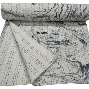 May include: A white and gray marble-patterned quilt with dark gray stitching. The quilt is folded and rolled, showcasing the intricate design. The overall theme is home decor.