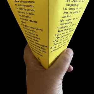 Puede incluir: Una linterna de papel amarilla con texto negro. El texto dice: "1. Ich geh mit meiner Laterne und meine Laterne mit mir. Da oben leuchten die Sterne hier unten da leuchten wir. St. Martin hier, wir leuchten dir rabimmel, rabammel, hmm. 2. Ich geh mit meiner Laterne und meine Laterne... Ein Lichtermeer zu Martina Enr rabimmel. mel, robumm. 1. Ich geh mit meiner Laterne maine Laterne Mein List schön, ihr könnt immel, 1. Die Laterne hat heut ihren großen Tag 2. die Laterne hat heut ihren großen Tag 3. die Laterne hat heut ihren, die Laterne hat heut ihren, 4. die Laterne hat heut ihren großen Tag 5. Anfangs war sie nur ein kleines Stück Popier 6. Dazu kam ein bisschen Farbe und ein Dra 7. Fine Kerze oor Farbe dann das Licht 8. Und so justiner Laternen"