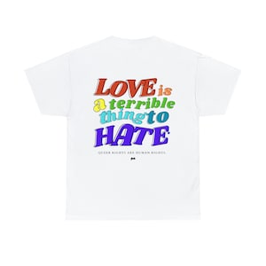 May include: White t-shirt with the text "LOVE is a terrible thing to HATE" in colorful, retro-style lettering. Below the text, it reads "QUEER RIGHTS ARE HUMAN RIGHTS." The shirt has a simple, classic design.