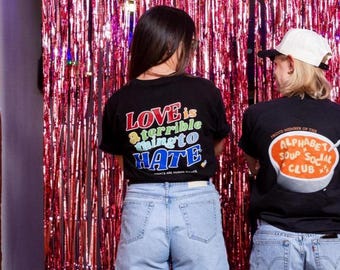 May include: Two black t-shirts with graphic prints and light blue denim shorts. The left shirt features the text LOVE is a terrible thing to HATE. The right shirt displays a bowl graphic with the text ALPHABET SOUP SOCIAL CLUB.