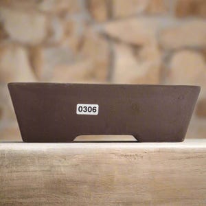 May include: A brown rectangular bonsai pot with a tapered design. The pot features a white sticker with the number "0306". The pot is on a wooden surface. Ideal for bonsai enthusiasts.