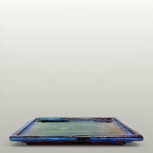 May include: A rectangular ceramic tray featuring a glossy, multi-toned glaze that transitions from a deep, dark blue along the raised edges to a muted, earthy green in the centre. The surface has a smooth, reflective finish with subtle variations.