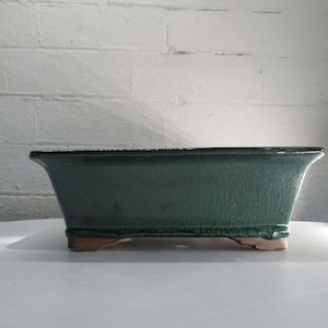 May include: A rectangular green ceramic bonsai pot with a textured glaze and four small feet.