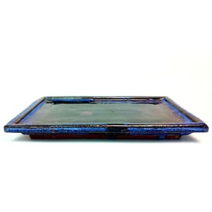 May include: A rectangular ceramic tray with a dark blue interior and a vibrant blue rim. The tray has a glossy finish and a reddish-brown base, creating a striking contrast against the white background. The tray is perfect for serving food or displaying decorative items.