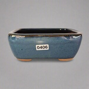 May include: A rectangular, blue ceramic bonsai pot with a dark rim and a light brown base. The pot has rounded corners and the number "0406" is printed on a white sticker on the front.