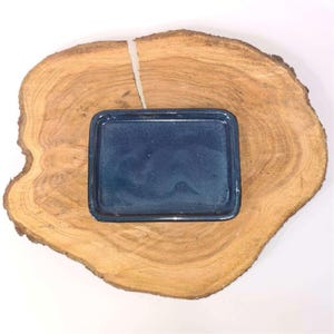 May include: A small, rectangular, blue ceramic dish on a wooden surface.