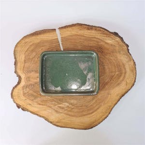 May include: A rectangular, green ceramic tray with a speckled surface sits on a round, natural wood slab. The wood has a light brown colour with visible grain patterns and a dark brown bark edge. The tray is centered on the wood, creating a rustic aesthetic.