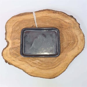 May include: A rectangular, dark grey metal tray with a slightly raised edge. The tray is set on a natural, light brown wooden slab with visible grain and a white crack. The wood has a rough, organic edge.